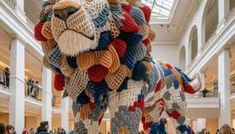 a large animal made out of knits in a building with lots of people walking around