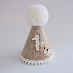 Say HELLO to our new addition - Beige Flecked Bear First Party Hat! Premium quality, handmade with love! Available with Custom Bear Topper as shown. Please select this option in the drop down, and enter name where required :) DETAILS ♕  1 x 100% Merino Wool Felt Party Hat. Finished with mini pom trim, bear face detail and wool Pom.  Elastic comes attached to wear around back of head. ♕ Size approx - Height 12cm, Width 8cm  Express post is also available in the shipping options. PLEASE NOTE Child Whimsical White Hat For Birthday, Cute White Hat For Birthday, Cute Cream Hat For Gift, White Cap For Birthday, Handmade Playful Party Hat, White Birthday Cap Hat, Playful Handmade Party Hat, Fun Handmade Hat For Birthday, Playful Birthday Cap Style Hat