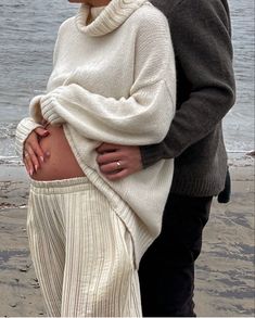 a man and woman standing next to each other on the beach with their stomach exposed