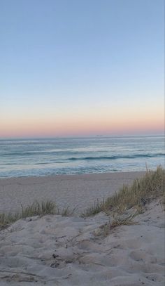 an empty beach with the ocean in the background and sand dunes to the side,