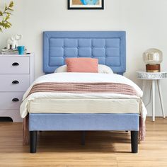 a bed with blue headboard in a white room next to a dresser and nightstand