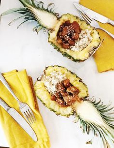 two pineapples with meat and rice in them on a white plate next to silverware