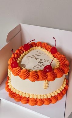 an orange and white birthday cake with cherries on the top is in a box