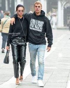 a man and woman walking down the street with headphones in their ears while wearing black sweatshirts