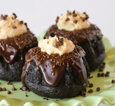 three chocolate desserts with white frosting and sprinkles on a green plate