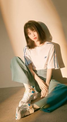 a woman sitting on the ground with her legs crossed, wearing adidas sneakers and a white t - shirt