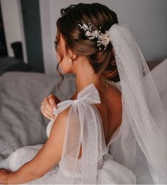 a woman sitting on top of a bed wearing a white dress and veil with flowers in her hair