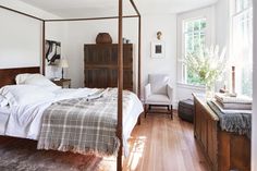 a bedroom with a four poster bed and white walls, hardwood flooring and windows