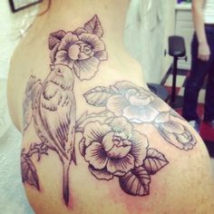 the back of a woman's shoulder with flowers and bird tattoo on her left side