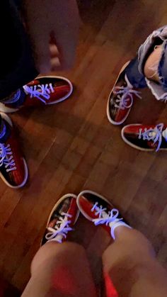 two people standing on top of a wooden floor next to red and blue shoes with white laces