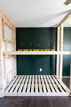 a bunk bed frame in the middle of a room with green walls and wood flooring