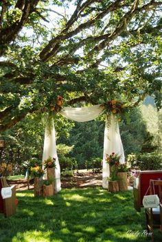 an outdoor ceremony setup with white draping and flowers on the arbor, surrounded by lush green grass