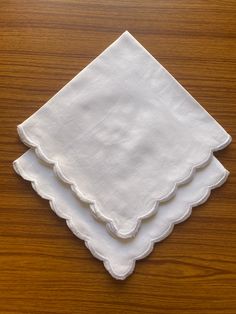 three white napkins with scalloped edges sitting on a wooden surface, one folded and the other unzipped