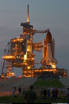 the space shuttle is lit up at night with people standing around and taking pictures in front of it