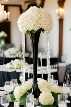 a tall black vase filled with white flowers on top of a table covered in crystal beads