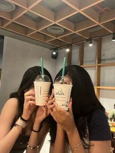 two women holding up starbucks cups in front of their faces