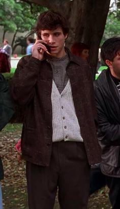 a man talking on a cell phone while standing next to other people in a park