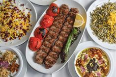 a table topped with plates filled with different types of food and meat on skewers