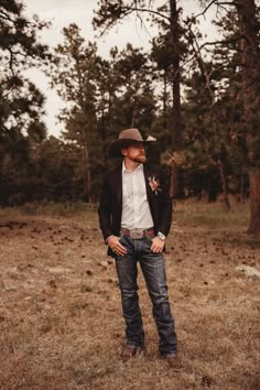 a man standing in the middle of a field wearing a cowboy hat and blue jeans