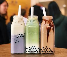 three milkshakes sitting on top of a wooden table