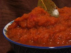 a blue and white bowl filled with red sauce on top of a wooden table next to a green leaf