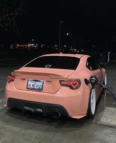 a pink car is parked in a parking lot at night with its gas pump out