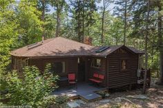 a small cabin in the woods with red chairs on the porch and trees around it