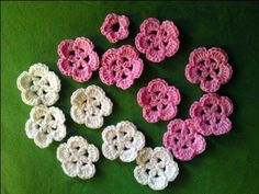 small crocheted flowers are arranged on a green surface with white and pink petals