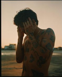 a man with tattoos covering his face and holding his hand up to his ear while standing on the beach