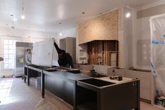 two men are standing in a kitchen with the cabinets up and one man is working on the wall