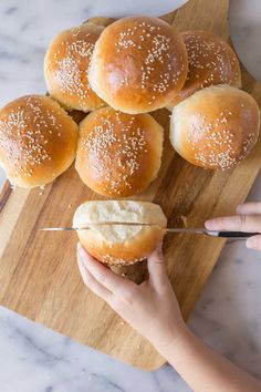 someone is cutting up the buns with a knife on a wooden board next to them