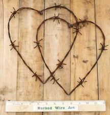 two heart shaped barbed wire on top of a wooden fence with the words barbed wire art written below it