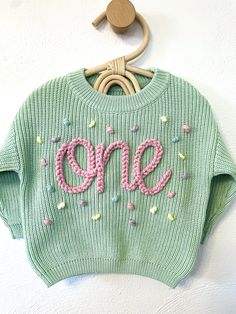 a green sweater with the word one written in pink and sprinkles on it