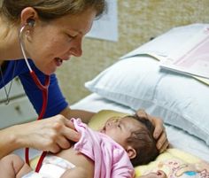 a woman in blue shirt and stethoscope examining a baby