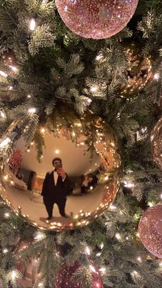 a christmas tree with ornaments and a man's reflection in the ornament