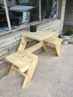 a wooden picnic table sitting in front of a window next to a potted plant