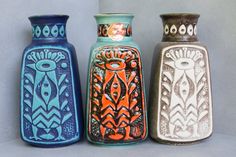 three different colored vases sitting next to each other on a counter top in front of a gray wall