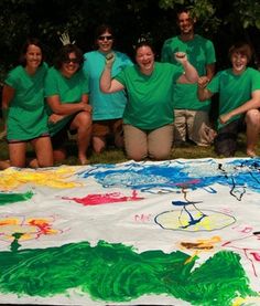 a group of people in green shirts are posing for a photo with a large painting on the ground