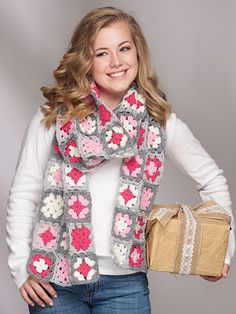 a woman holding a brown bag and wearing a crocheted scarf with flowers on it