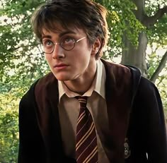 a young man wearing glasses and a tie in front of some trees with green leaves