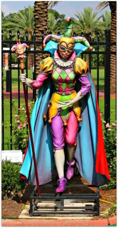 a statue of a man dressed as a clown holding a cane in front of a fence