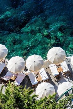 an aerial view of umbrellas and lounge chairs on the beach with clear blue water in the background