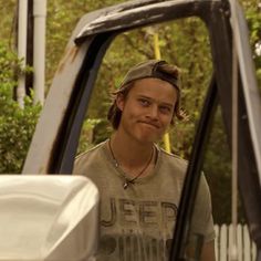 a young man standing in the driver's seat of a truck looking at the camera