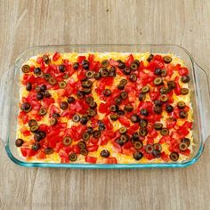 a casserole dish with tomatoes, olives and cheese in it on a wooden table