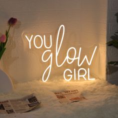 a neon sign that says you glow girl next to a vase with tulips