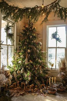 a decorated christmas tree sitting in front of two windows with lit candles on the floor