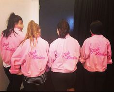 four women in pink jackets are standing near a black wall and one woman is looking at the mirror