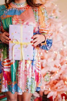 a woman holding a present in front of a christmas tree