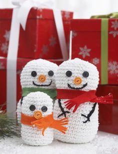 two crocheted snowmen standing next to each other with presents in the background