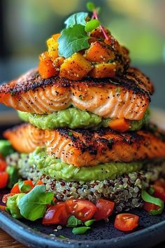 salmon with guacamole, tomatoes and other vegetables on a black plate sitting on a wooden table